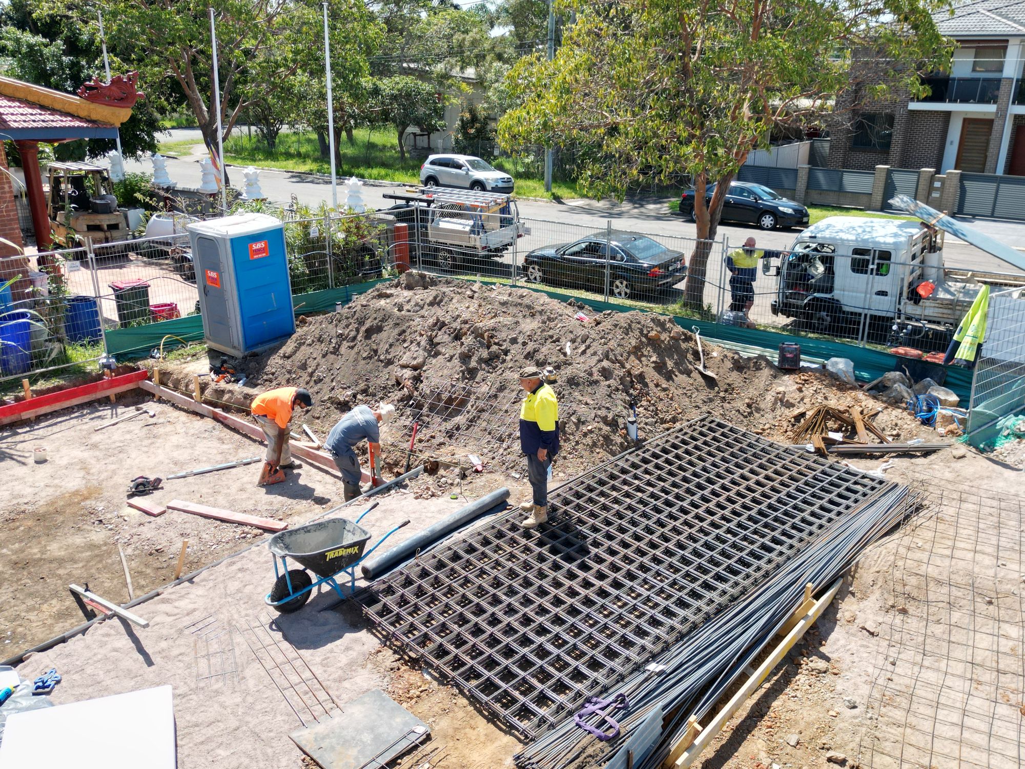Crew setting red edge formwork with stacked reinforcement mesh sheets and starter bars delivered alongside.